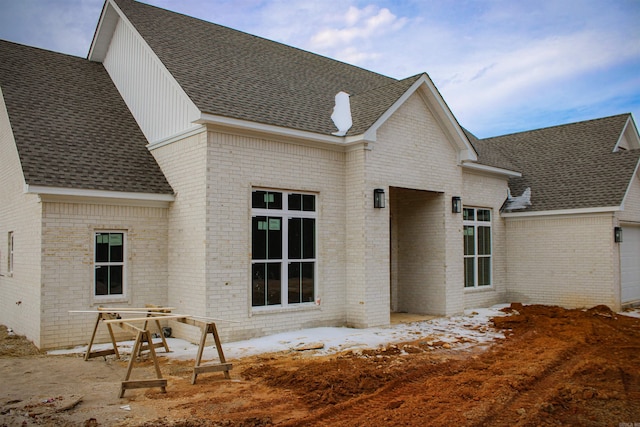 rear view of property with brick siding and roof with shingles