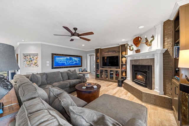 living area with recessed lighting, a tiled fireplace, ornamental molding, a ceiling fan, and light wood-type flooring