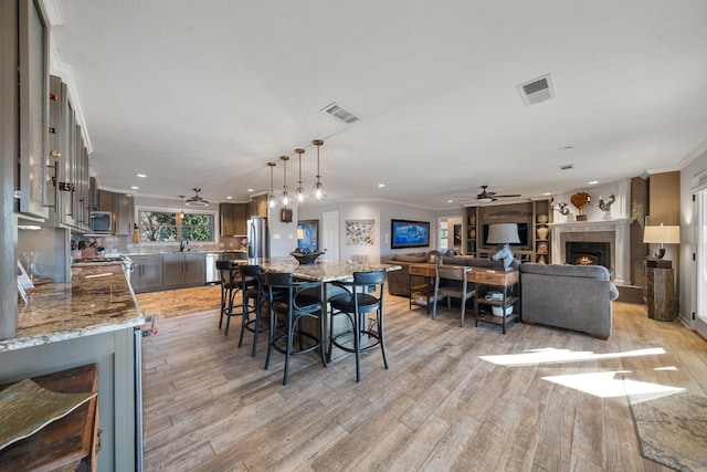 dining space with a warm lit fireplace, ornamental molding, light wood-type flooring, and visible vents