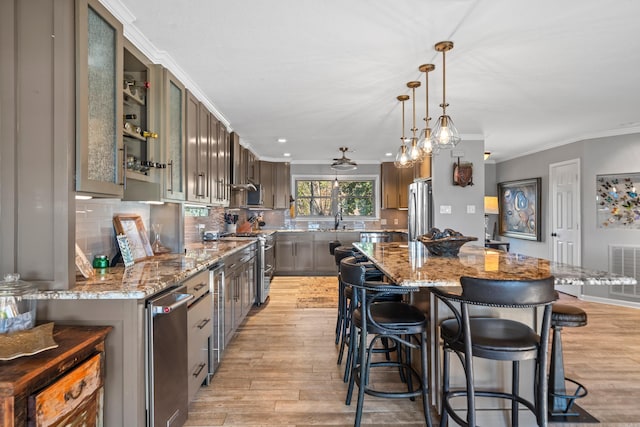 kitchen featuring light stone counters, stainless steel appliances, a spacious island, hanging light fixtures, and glass insert cabinets