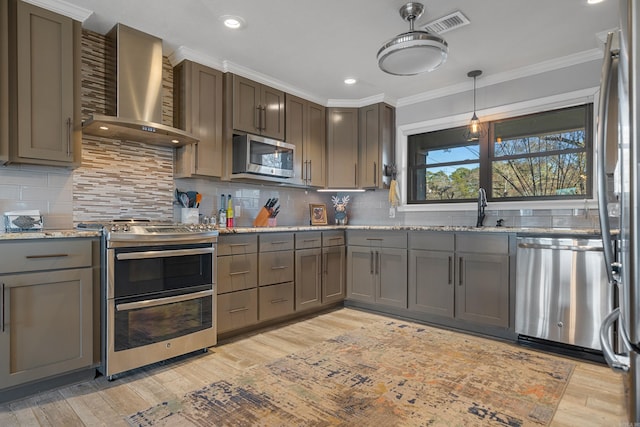 kitchen with a sink, wall chimney range hood, appliances with stainless steel finishes, light stone countertops, and crown molding