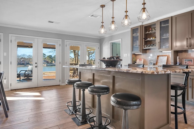 bar with a water view, visible vents, decorative light fixtures, and french doors