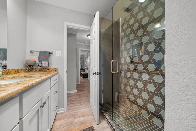 full bath with a textured wall, wood finished floors, vanity, baseboards, and a shower stall