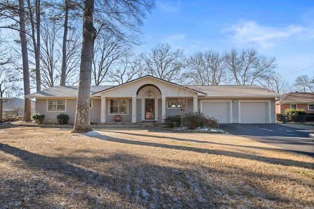 ranch-style house featuring aphalt driveway, a standing seam roof, metal roof, and a garage