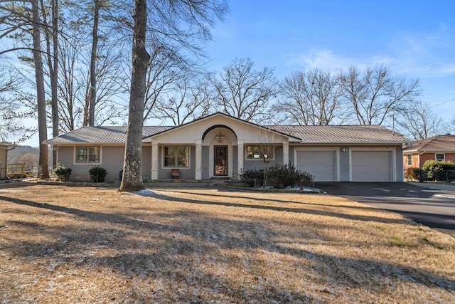 view of front of property with aphalt driveway, an attached garage, a standing seam roof, metal roof, and a front lawn