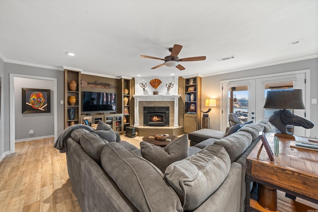 living area with french doors, crown molding, visible vents, wood finished floors, and a lit fireplace