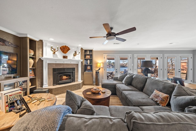 living area with visible vents, a tiled fireplace, ornamental molding, wood finished floors, and french doors