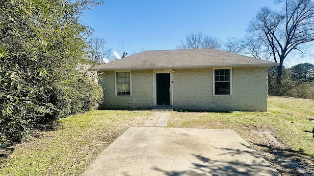 bungalow featuring roof with shingles, concrete block siding, a front lawn, and a patio