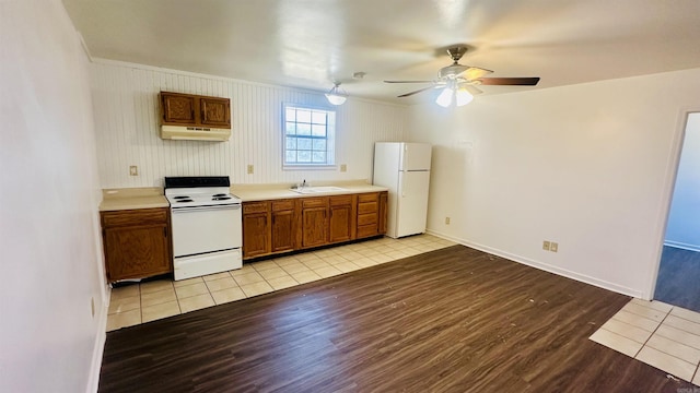 kitchen featuring white appliances, brown cabinets, light countertops, light wood-type flooring, and under cabinet range hood