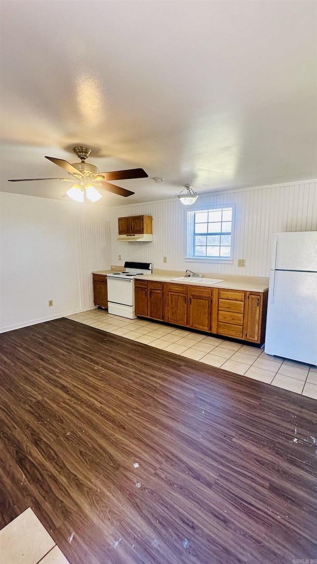 kitchen with brown cabinets, light wood finished floors, light countertops, a sink, and white appliances