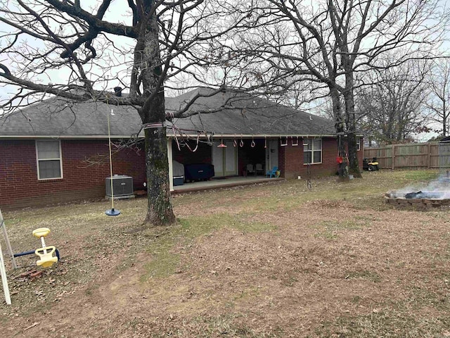 rear view of property with a shingled roof, brick siding, fence, and central air condition unit