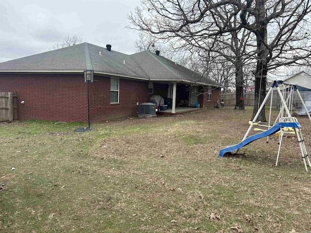 exterior space featuring a playground, central AC, brick siding, fence, and a yard