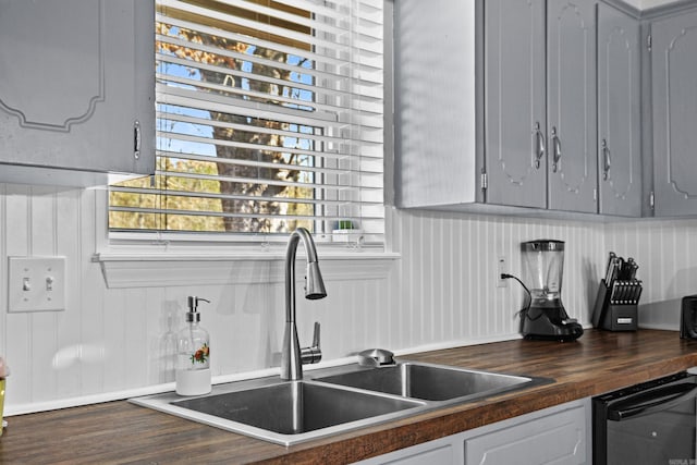 kitchen with butcher block countertops, black dishwasher, a sink, and gray cabinetry