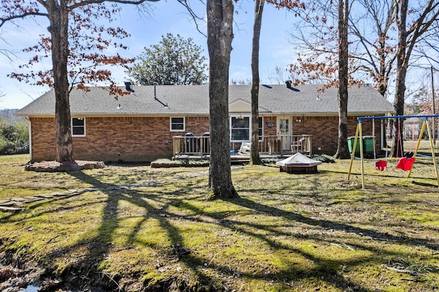 rear view of house featuring a wooden deck, roof with shingles, a yard, a playground, and brick siding