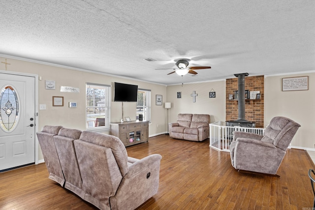 living room featuring a wood stove, a textured ceiling, ornamental molding, and wood finished floors