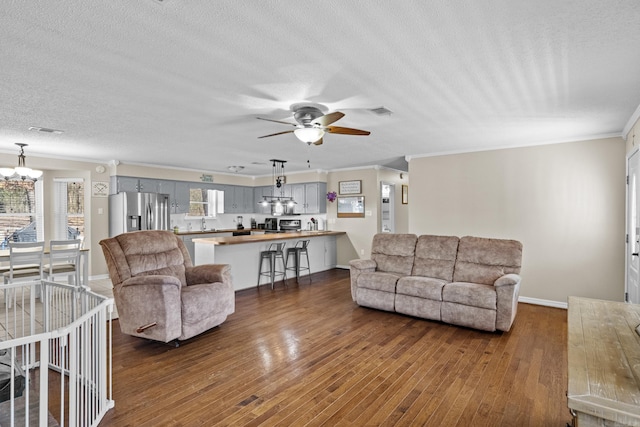 living area with dark wood-style floors, ornamental molding, a textured ceiling, and visible vents