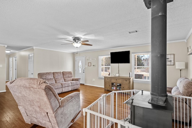 living area featuring visible vents, wood finished floors, a wood stove, and crown molding