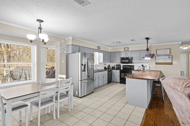 kitchen featuring butcher block countertops, a sink, visible vents, black appliances, and decorative light fixtures