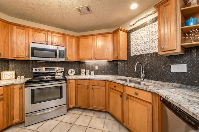 kitchen with stainless steel appliances, brown cabinets, a sink, and light stone counters