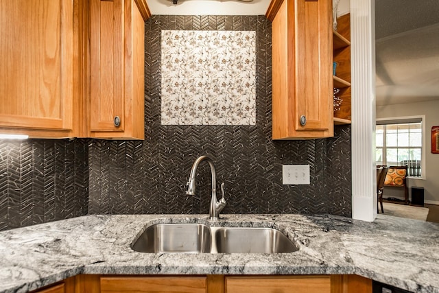 kitchen with brown cabinets, light stone countertops, decorative backsplash, and a sink