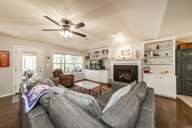 living room featuring ceiling fan, a textured ceiling, wood finished floors, and a glass covered fireplace