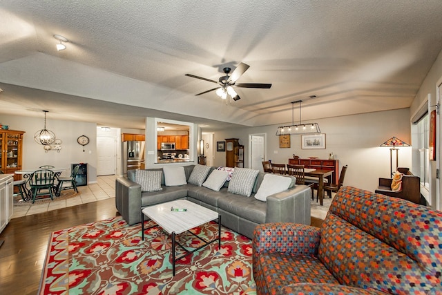 living area with light wood-type flooring, a textured ceiling, and ceiling fan with notable chandelier