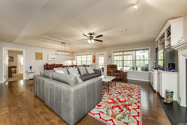 living room with dark wood finished floors, visible vents, ceiling fan, a textured ceiling, and baseboards