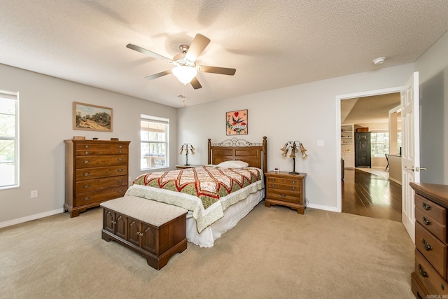 bedroom featuring light carpet, ceiling fan, baseboards, and a textured ceiling