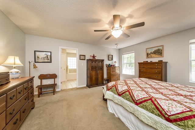 bedroom featuring baseboards, light colored carpet, ensuite bath, ceiling fan, and a textured ceiling