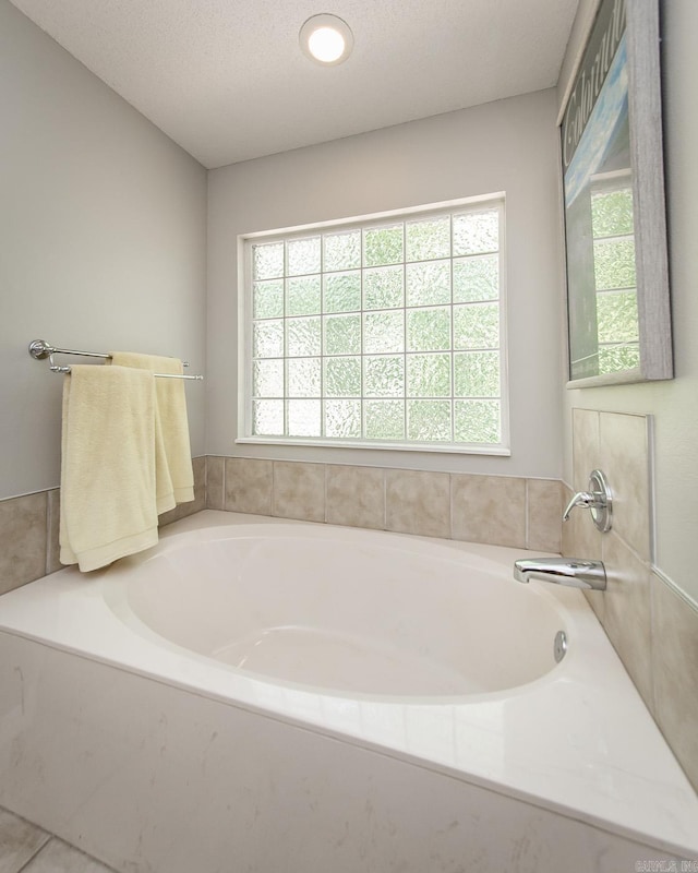 full bathroom with a wealth of natural light, a textured ceiling, and a bath