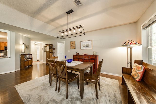 dining space featuring dark wood-style floors, visible vents, a textured ceiling, and baseboards