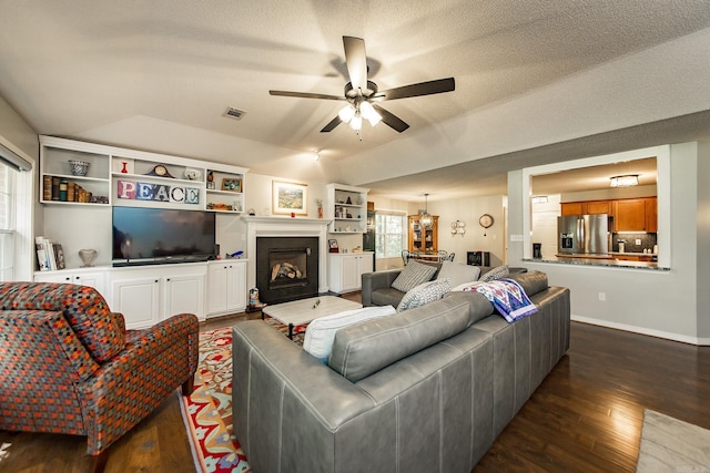 living room with lofted ceiling, a fireplace with raised hearth, ceiling fan, dark wood-style flooring, and visible vents