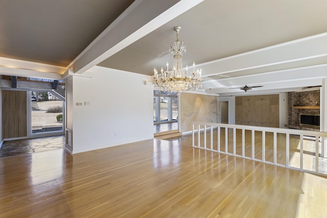 spare room featuring a large fireplace, wood finished floors, beamed ceiling, baseboards, and ceiling fan with notable chandelier