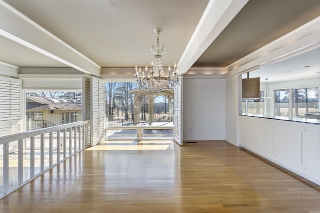 unfurnished dining area featuring ornamental molding, light wood-type flooring, and a notable chandelier