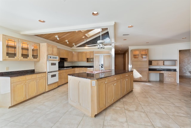 kitchen with a center island with sink, glass insert cabinets, dark stone countertops, double oven, and a sink