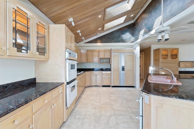 kitchen featuring a skylight, glass insert cabinets, paneled built in refrigerator, light brown cabinets, and a sink