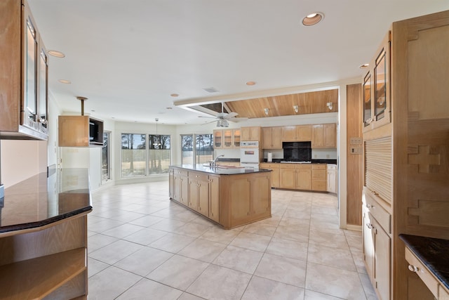 kitchen featuring pendant lighting, a center island with sink, dark countertops, glass insert cabinets, and light brown cabinets