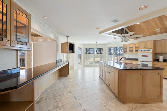 kitchen featuring a large island, dark countertops, glass insert cabinets, double oven, and a sink