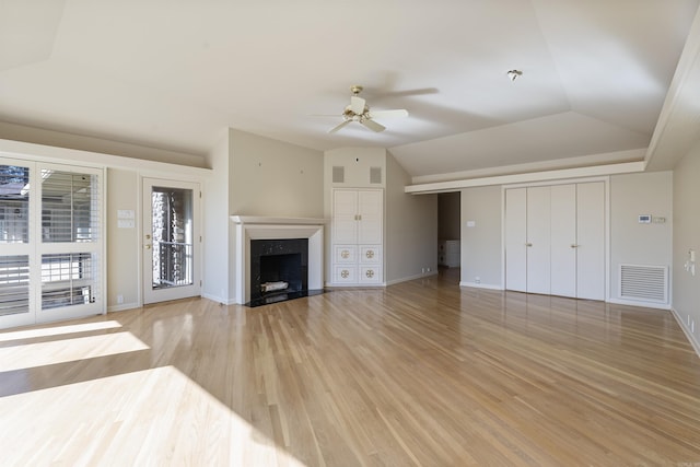 unfurnished living room with lofted ceiling, a high end fireplace, visible vents, and light wood-style flooring