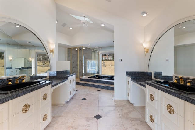 bathroom featuring a bath, lofted ceiling with skylight, two vanities, and a sink