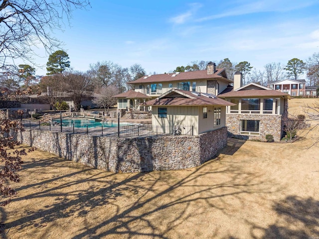 back of house featuring stone siding, a chimney, a fenced in pool, and a yard