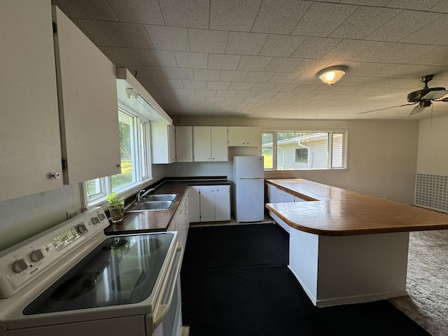 kitchen featuring dark countertops, white cabinets, a sink, white appliances, and a peninsula