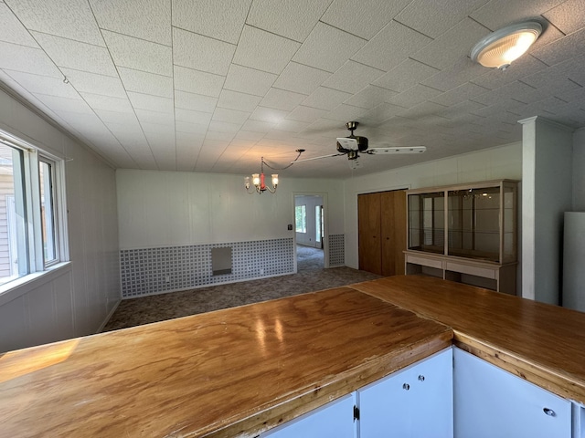 interior space with open floor plan, butcher block countertops, ceiling fan with notable chandelier, and carpet