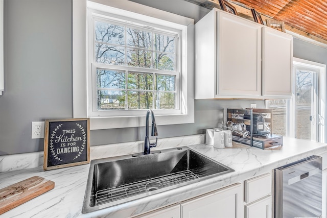 kitchen featuring light stone countertops, dishwasher, white cabinetry, and a sink