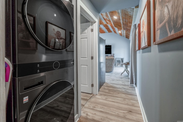 corridor featuring lofted ceiling, baseboards, light wood finished floors, and stacked washing maching and dryer