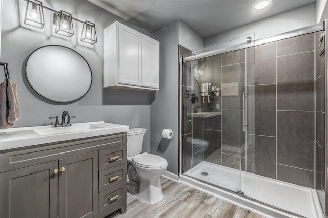 bathroom featuring baseboards, toilet, wood finished floors, vanity, and a shower stall