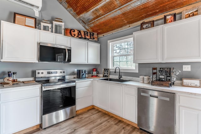 kitchen with white cabinets, a wall mounted air conditioner, stainless steel appliances, light countertops, and a sink