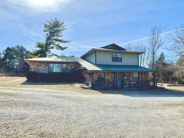 view of front facade with driveway, stone siding, metal roof, and a porch