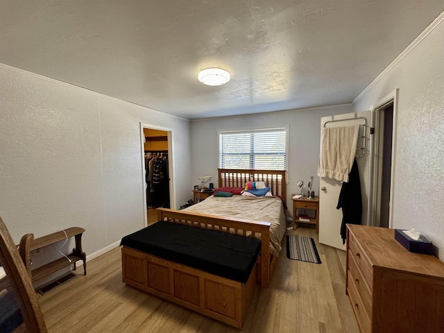 bedroom featuring light wood-style flooring, a spacious closet, crown molding, and a textured wall