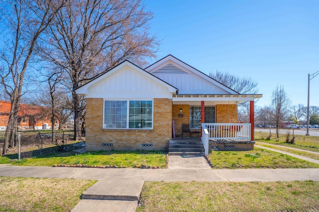 bungalow with brick siding, a porch, a front yard, crawl space, and fence